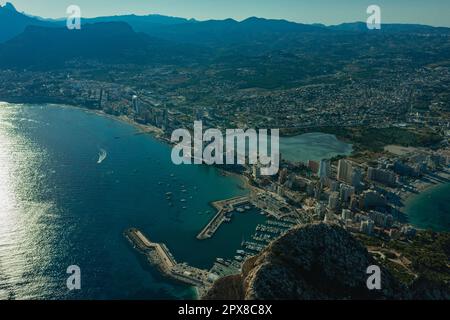 Luftaufnahme atemberaubende Penyal dIfac Naturpark von Penon de Ifach massiven Kalkstein auf dem Mittelmeer, vertäute Schiffe im Hafen von Calpe. Sunn Stockfoto