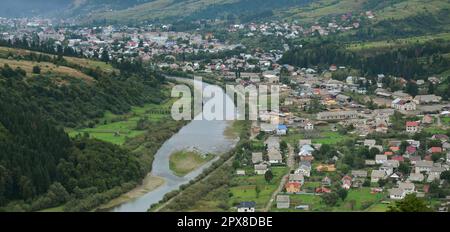 Eine wunderschöne Aussicht auf das Dorf Mezhgorye, Karpaten Region. Eine Menge von Wohngebäuden durch hohe Wald Berge und lange Fluss umgeben Stockfoto