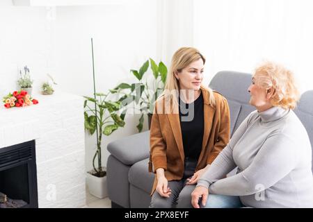 Nahaufnahme gealterte Mutter Erwachsene Tochter, die drinnen auf dem Sofa sitzt und lächelt und für die Kamera posiert, fühlt sich glücklich an, Zeit miteinander zu verbringen, Concept Stockfoto