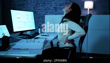 Junge Geschäftsfrau, die mit Schmerzen im Rücken beim Sitzen am Schreibtisch Stockfoto
