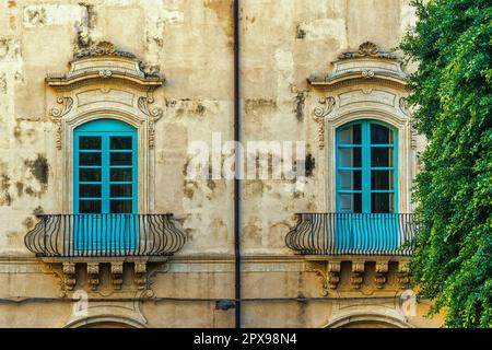 Zwei blaue Fenster mit barocken Dekorationen in einem antiken Gebäude in der Stadt Noto. Noto, Provinz Syrakus, Sizilien, Italien, Europa Stockfoto