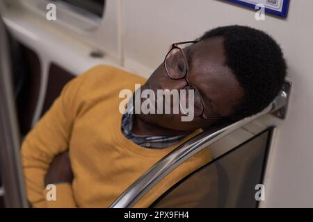 Müder junger Mann mit Brille, der während seiner Reise im U-Bahn-Auto schläft Stockfoto