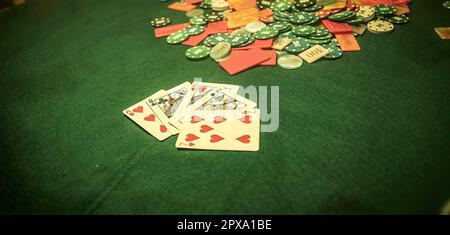 Eine chaotische Szene eines Pokerspiels mit Chips, die willkürlich über den Tisch verteilt sind. Verschwommener Hintergrund eines Pokerspielers, der am Tisch sitzt. Stockfoto