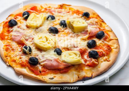 Pizza mit Schinken, schwarzen Oliven und Artischocken Stockfoto