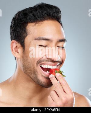 Erdbeeren sind einfach unwiderstehlich. Ein Mann, der vor einem grauen Hintergrund eine Erdbeere beißt. Stockfoto