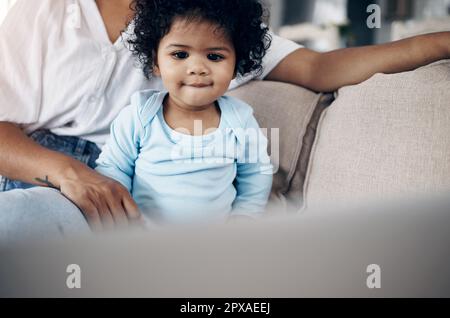 Das sieht interessant aus. Eine nicht wiedererkennbare Frau, die einen Laptop mit ihrer Tochter zu Hause auf dem Sofa benutzt. Stockfoto