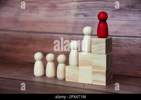 Die rote Figur auf Holzblöcken führt andere Figuren zum Erfolg. Konzept für Führungsqualitäten und Unternehmenskultur. Stockfoto