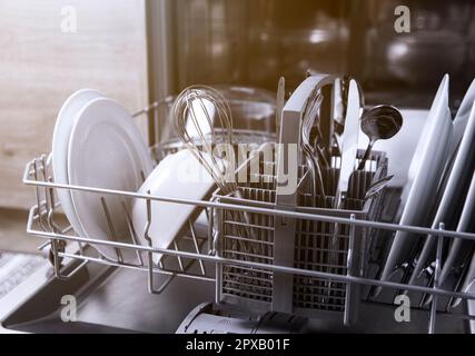 Vorderansicht der offenen automatischen Edelstahl-Einbaumaschine mit vollständig integrierter Steuerung der oberen Spülmaschine mit sauberen Utensilien, Besteck, Gläsern und DIS Stockfoto