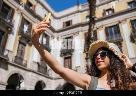 Junge indische Touristinnen mit Strohhut und Sonnenbrille, die sich am Marktplatz selbst fotografieren Stockfoto