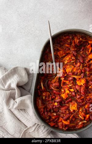 Gesundes Frühstück und Mittagessen, gedünstete rote Bohnen mit Karotten, Zwiebeln und Tomaten, Blick von oben auf eine ovale Keramikrösterei mit gedünsteten Hülsenfrüchten Stockfoto