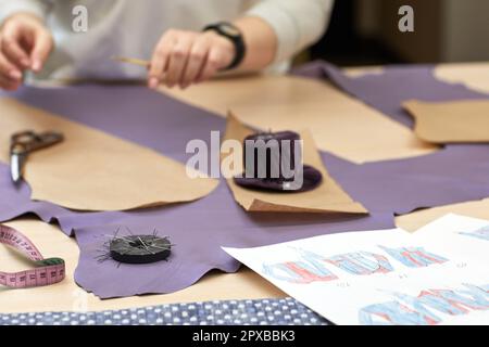 Arbeitsplatz der Näherin. Schneiderin schneidet Textil auf den Skizzenlinien. Weibliche Hand mit der Schere schneiden Stoff. Stockfoto