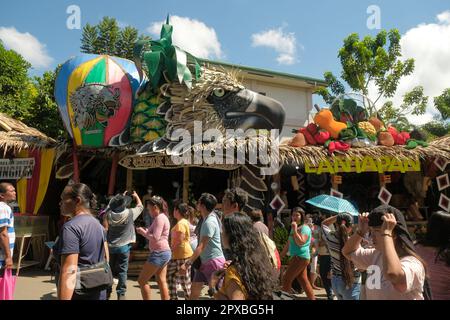 Malaybalay City, Philippinen: Die Menschen gehen auf einer belebten Straße mit dekorierten Nipa-Hütten als Pop-up-Geschäfte, die beim Kaamulan Festival in Bukidnon einheimische Waren verkaufen. Stockfoto