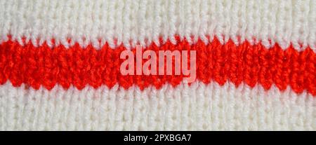 Gemusterter Stoff aus Wolle. Handgefertigtes Strickmaterial mit roter und weißer Wollhintergrundstruktur Stockfoto