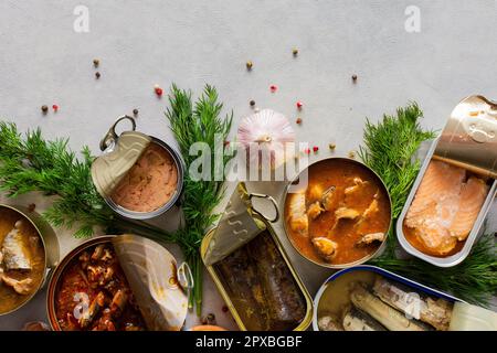 Verschiedene offene Blechdosen mit Fischkonserven unter Gewürzen und Kräutern, Lachs- und Makrelenkonserven, Sprotte und Sardine, Thunfisch und Hering sowie Fischpastete Stockfoto