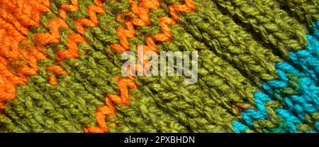 Gemusterter Stoff aus Wolle. Handgefertigtes Strickmaterial: Türkisfarbene orange- und grüne Wollhintergrundstruktur Stockfoto