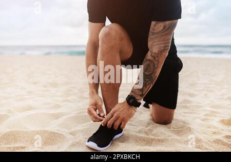 Mann in Sportbekleidung bindet Schnürsenkel seiner Schuhe, während er am Strand joggt, Nahaufnahmen von Beinen, kurze Aussicht Stockfoto