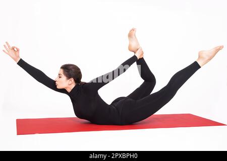 Hübsches, sportliches Mädchen im schwarzen Anzug, das Yoga macht. Naukasana asana Boot Pose. Isoliert auf weißem Hintergrund. Stockfoto