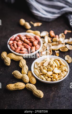 Ungeschälte und geschälte Erdnüsse in der Schüssel auf dem Küchentisch. Stockfoto