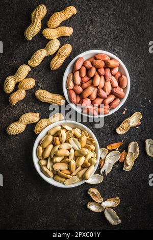 Ungeschälte und geschälte Erdnüsse in der Schüssel auf dem Küchentisch. Draufsicht. Stockfoto