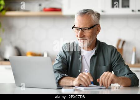 Remote-Arbeit Bei Ausscheiden. Senior Man Verwendet Laptop In Der Küche Zu Hause Stockfoto