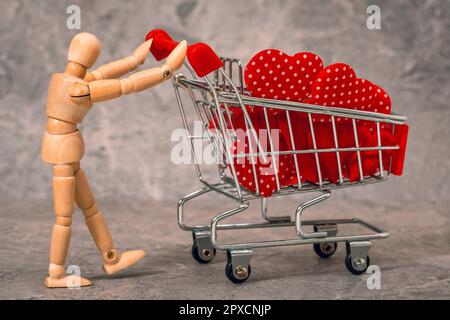 Schaufensterpuppe aus Holz, die einen Einkaufswagen voller Herzen zum Valentinstag schiebt Stockfoto