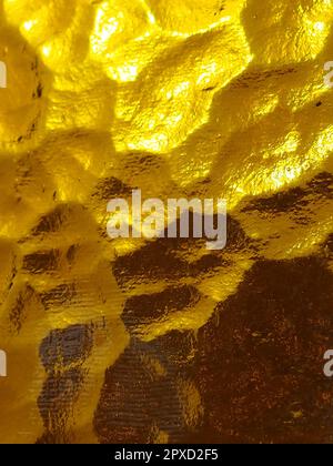 goldgelbes Wellglas mit hellem und dunklem Hintergrund. Lichtreflexionen. Wellglas, Rücklichtquelle. Spiel von Blendung und Reflekti Stockfoto