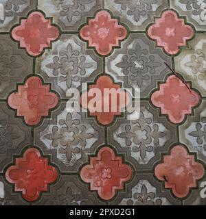 Eine Kopfsteinpflasterstraße oder Straße mit quadratischen und abgerundeten dekorativen Betonfliesen in Grau und Rot. Steinstruktur. Geometrisches Ostmuster auf dem Boden. Stockfoto