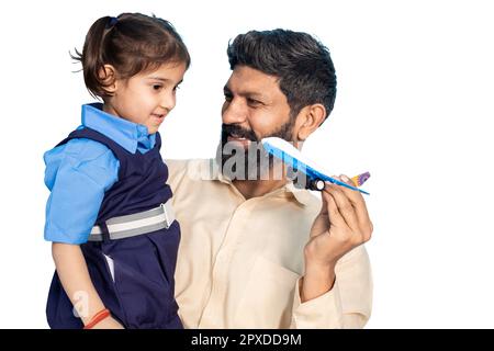 Junger indischer Vater und kleines Mädchen in Schuluniform, die mit einem Spielzeugflugzeug spielen, isoliert vor weißem Hintergrund. Ländliches indien. Stockfoto