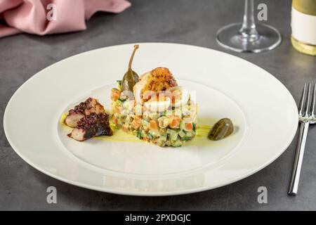 Russischer Salat mit Aioli-Sauce, Garnelen, Tintenfisch und Kapern auf einem weißen Porzellanteller Stockfoto