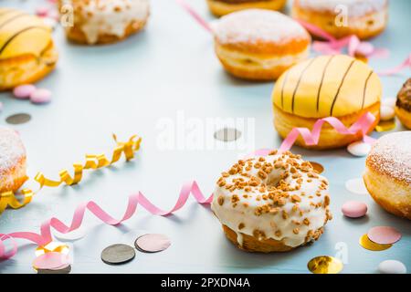 Deutsche Krapfen oder Donuts mit Bändern und Konfetti. Traditioneller Berliner für Karneval und Party. Farbenfrohes Karneval- oder Geburtstagsbild Stockfoto