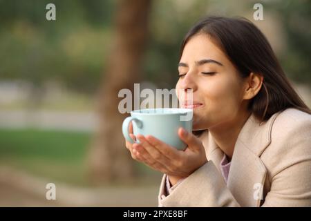 Eine Frau bei Sonnenuntergang im Winter, die Kaffee in einem Park riecht Stockfoto