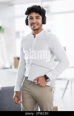 Professionelle Kleidung muss keinen Anzug beinhalten. Porträt eines jungen Geschäftsmannes, der Kopfhörer trägt und ein Notebook in einem Büro hält. Stockfoto