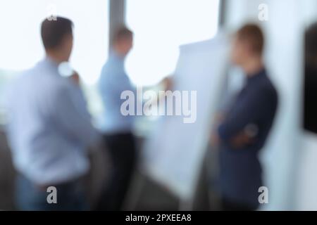 Ein verschwommenes Bild von drei Geschäftsleuten in einem professionellen Meeting, bei dem Details eines Projekts besprochen werden Stockfoto