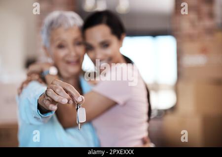 Was ein Zuhause ausmacht, sind die Erinnerungen, die darin gemacht werden. Eine ältere Frau, die neben ihrer Tochter steht und die Schlüssel zu ihrem neuen Zuhause hochhält. Stockfoto