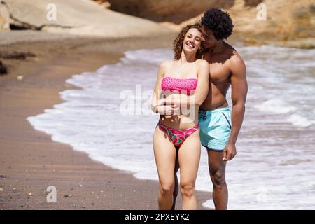 Glückliches, vielfältiges Paar, das sich am Strand umarmt Stockfoto