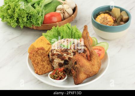 Nasi NACH OR Tutug Oncom. Traditioneller Sundanesischer Reis gemischt mit fermentierten Sojabohnen, begleitet von gebratenem Huhn, Tempeh, Tofu, Gemüse, Sambal, Sag Schon Stockfoto