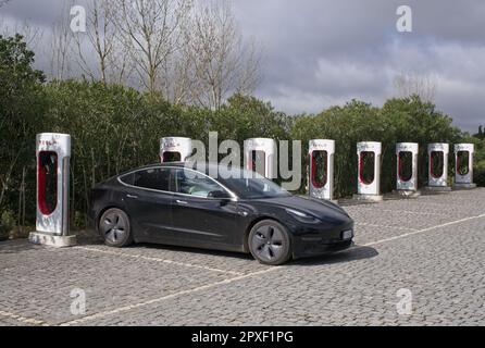 Montemor-o-Novo, Portugal - 1. April 2023: Statische Aufnahme eines soliden schwarzen Tesla Model 3 Dual Motor, der am Montemor-o-Novo Supercharger in A s aufgeladen wird Stockfoto