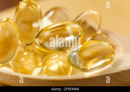 Gelbölhaltige Weichgelkapseln auf Holzhintergrund. Kosmetikpillen-Kapsel aus Vitamin E, A, Mandelöl, Omega 3, Fisch. Stockfoto