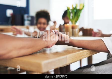 Eine Familie, die zusammen betet, zusammenbleibt. Eine nicht wiedererkennbare Familie, die während der Gebetszeit zu Hause Händchen hält. Stockfoto