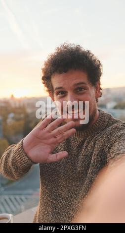 Ein lächelnder Typ steht morgens auf dem Balkon und macht Selfie auf dem Smartphone Stockfoto