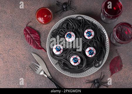 Halloween italienische schwarze Pasta dekorierte Horroraugen auf grauem Teller, Draufsicht Stockfoto