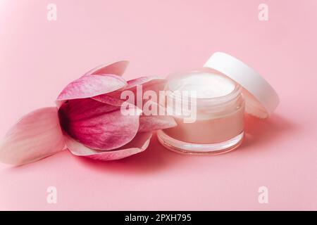 Kosmetische Cremedose und Magnolienblüte auf pinkfarbenem Hintergrund. Hautpflege, Schönheitsbehandlungskonzept. Nahaufnahme. Stockfoto