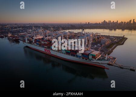 Luftaufnahme eines großen Containerschiffs OOCL, das an einem belebten Hafen angelegt ist, mit anderen Schiffen im Hintergrund Stockfoto