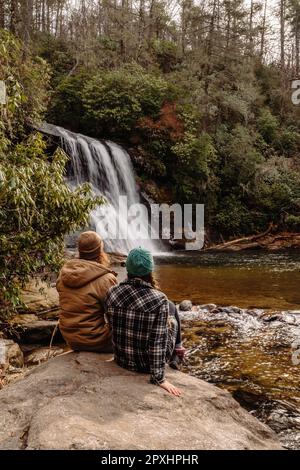 Die beiden Leute sitzen auf einem Felsen mit einem Wasserfall im Hintergrund. Stockfoto