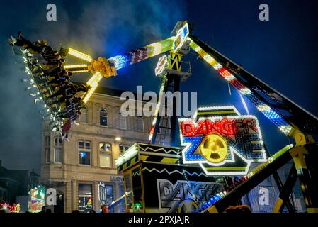 Fahrspaß auf dem Festgelände, bei dem die Menschen hoch auf einem Kranarm hochgehoben und umhergeschleudert werden. Abendliche lustige, faire Fahrt. England Großbritannien Stockfoto