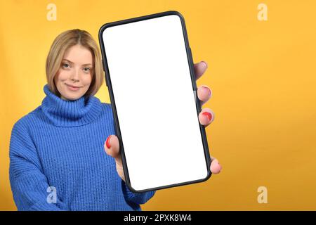 Ein positiver Millennials mit Smartphone und weißem, leerem Bildschirm auf farbenfrohem Studiohintergrund Stockfoto