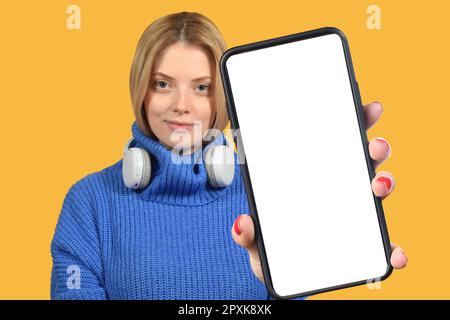 Ein positiver Millennials mit Smartphone und weißem, leerem Bildschirm auf farbenfrohem Studiohintergrund Stockfoto