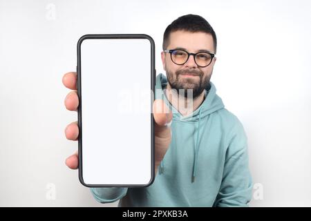 Ein junger Mann mit Brille und Bart zeigt ein Telefon mit einem leeren weißen Bildschirm Stockfoto