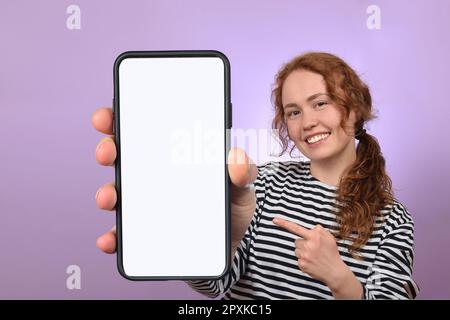 Ein positiver Millennials mit Smartphone und weißem, leerem Bildschirm auf farbenfrohem Studiohintergrund Stockfoto