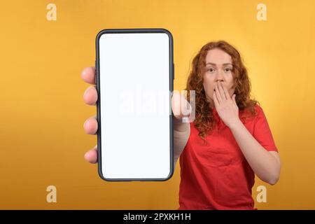 Ein positiver Millennials mit Smartphone und weißem, leerem Bildschirm auf farbenfrohem Studiohintergrund Stockfoto